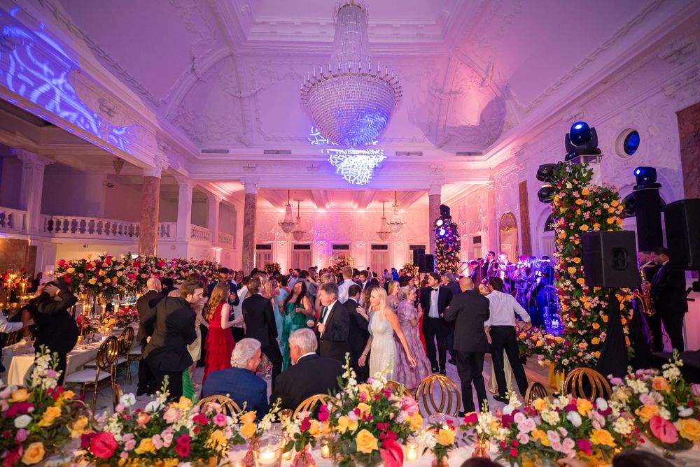 A grand ballroom decorated with colorful floral arrangements and chandeliers hosts an elegant evening event.