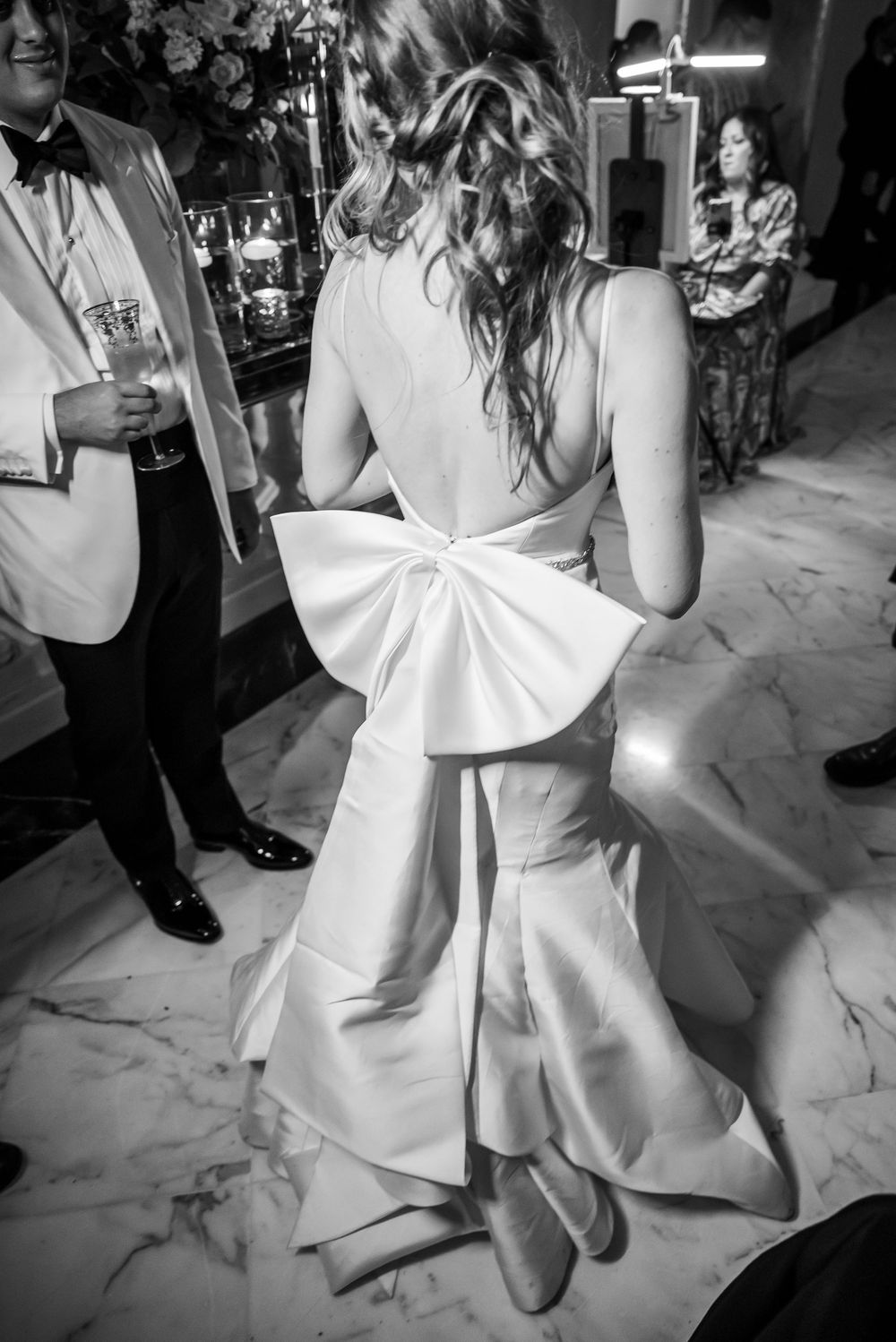 Elegant wedding dress with a dramatic bow detail on the back shown in black and white at an upscale reception.