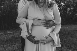 Black and white intimate maternity photo showing embrace of pregnant belly while wearing long sleeve dress outdoors.