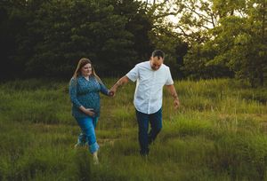 Two people in blue and white outfits hold hands while walking through a grassy hillside during golden hour.