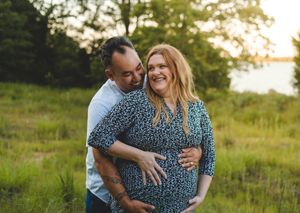 A couple shares an intimate moment in a sunlit field during a maternity photo session at sunset.