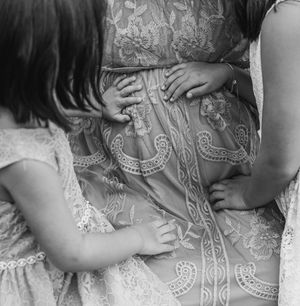 Black and white photo of children touching a pregnant woman's belly in a lace maternity dress.
