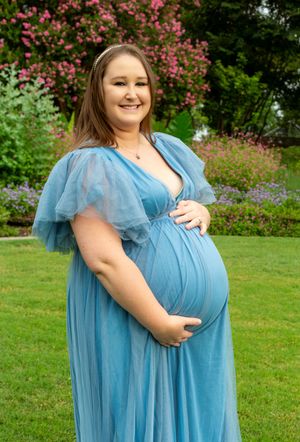 Light blue flowing maternity photoshoot dress captured in a garden setting with pink flowers in background.