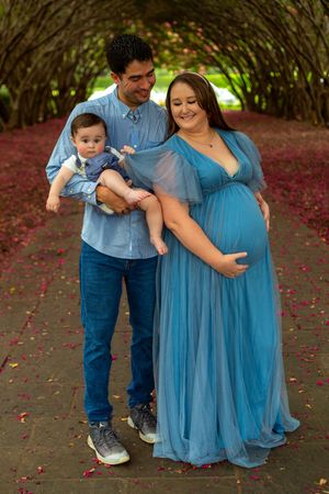 A family poses under an arched garden pathway with red petals scattered on the ground, wearing coordinating blue outfits.