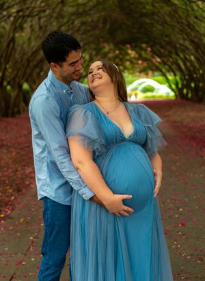 A loving couple shares an intimate moment under a natural archway, with the woman wearing a flowing blue maternity gown.