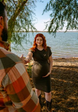 Couple enjoying a peaceful moment by a lakeside under drooping willow trees on a sunny afternoon.