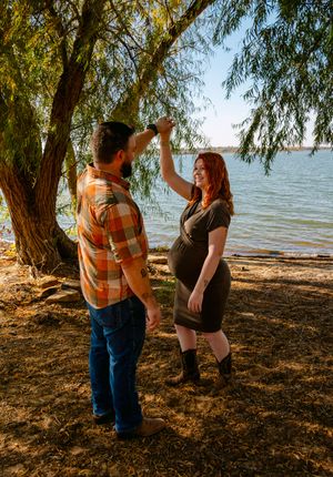 A couple shares tender moments under a willow tree by the lake on a sunny afternoon.
