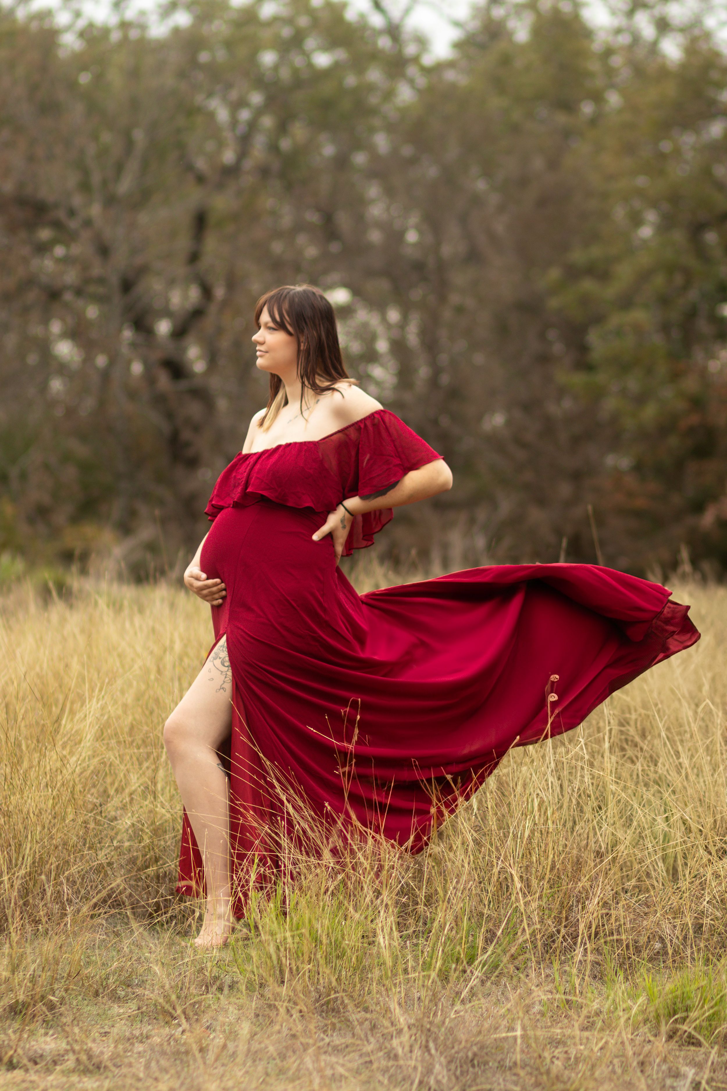 A flowing red maternity dress catches the wind in a golden field during sunset.