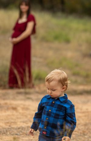 A toddler in a blue plaid shirt explores while someone in red stands in the background.