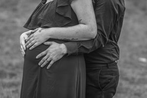 An intimate black and white photo showing hands cradling a pregnant belly.
