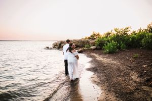 Couple sharing a romantic embrace on a rocky shoreline at sunset during their beach wedding photo session.