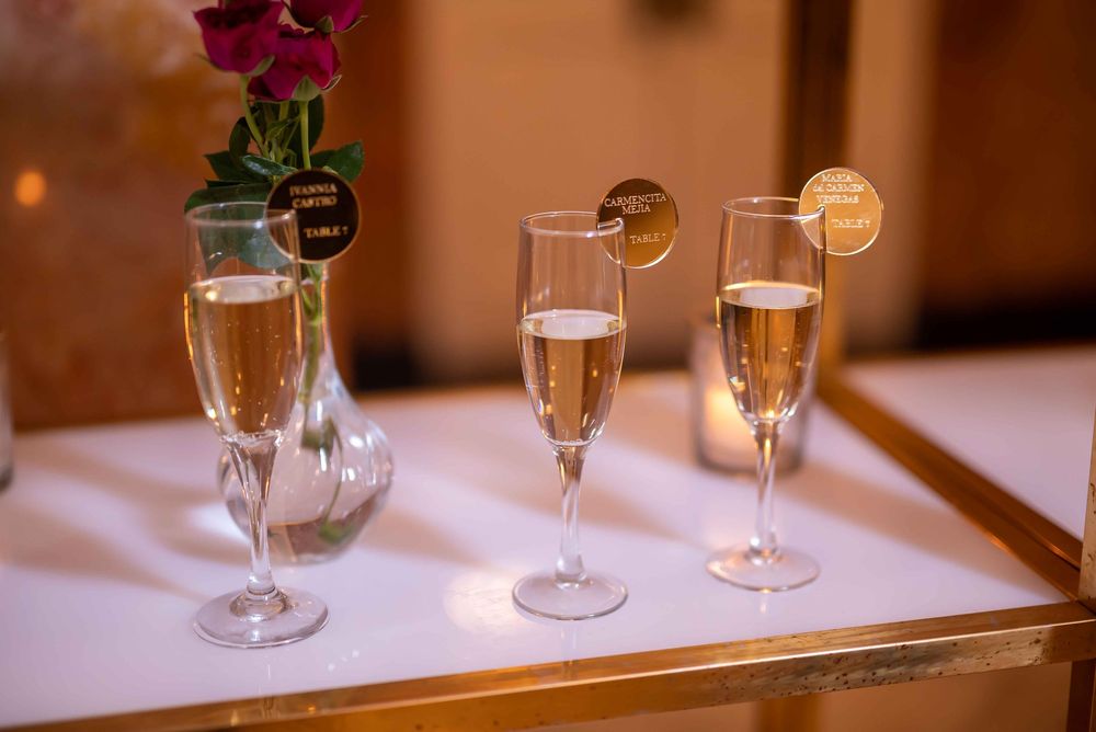 Three champagne flutes with orange garnish slices sit on a white tray alongside a small red flower in a vase.