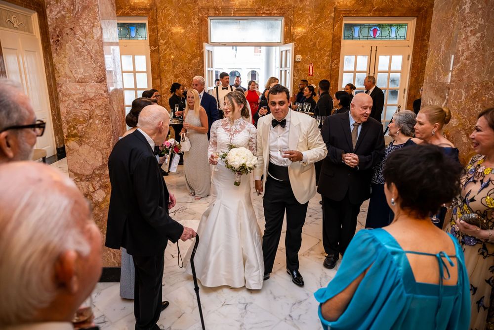 Wedding guests gather in an elegant marble-walled venue hallway during a reception celebration.
