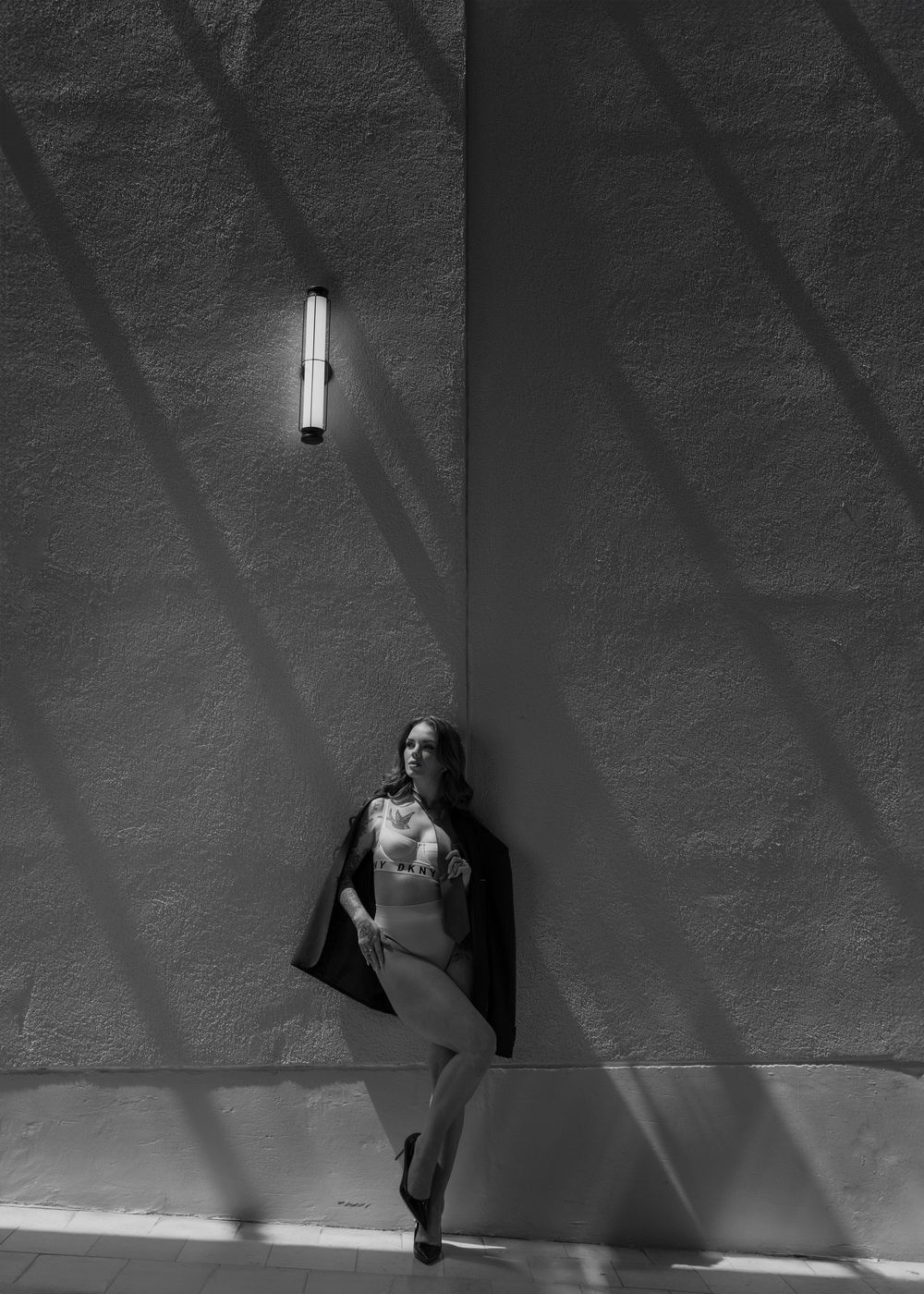 A monochromatic image of a dancer posing against a textured wall with dramatic diagonal shadows.