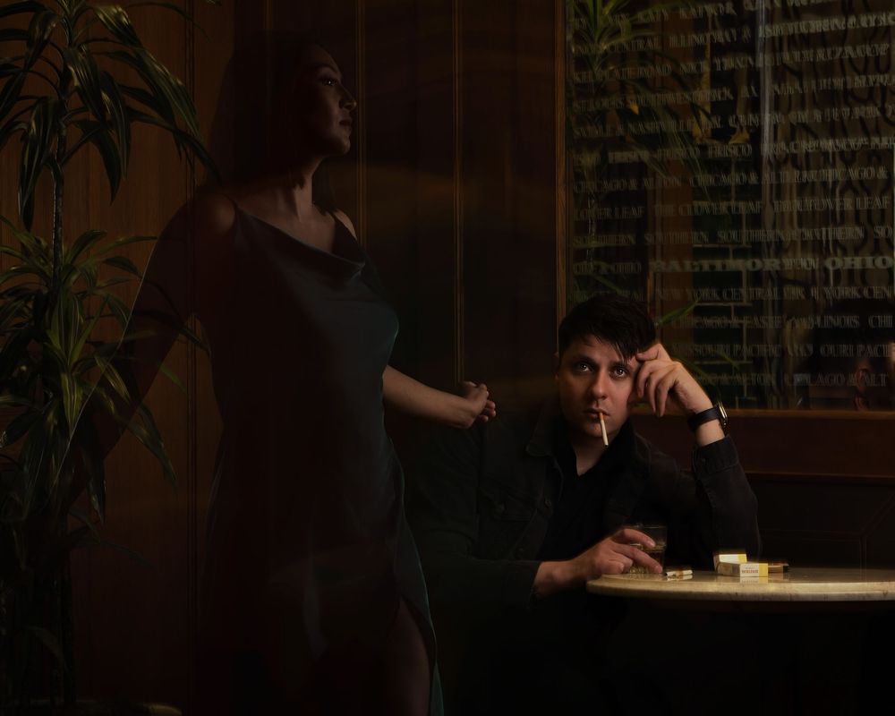 A moody scene at a cafe table with dramatic lighting, warm tones and houseplants in the background.