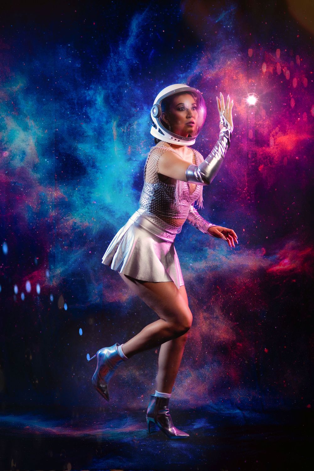 Figure in white dress and astronaut helmet poses against cosmic nebula backdrop with vibrant blue and pink lighting effects.