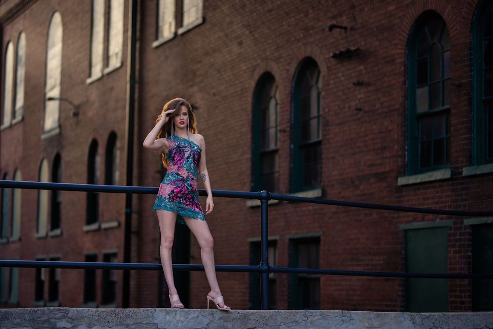 Athletic figure poses in summer outfit against urban brick building backdrop in natural sunlight.