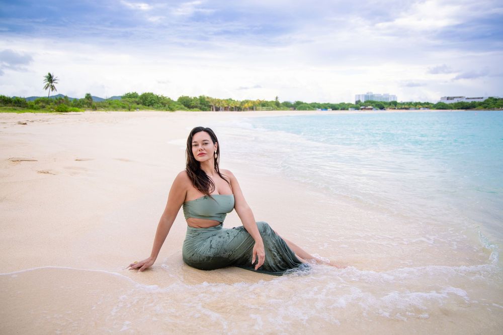 Turquoise dress-clad beachgoer relaxes in gentle waves on pristine sandy beach with palm trees and blue water. Saint Maarten