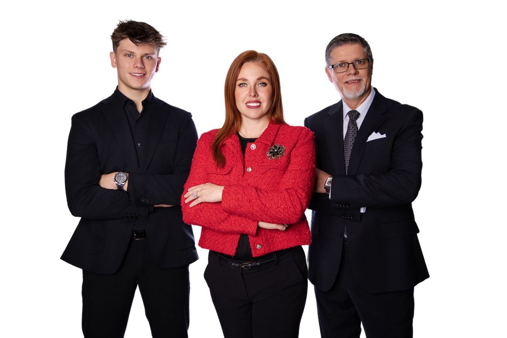 Three business professionals in formal attire standing with arms crossed against white background.