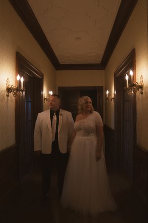 A wedding couple walks through a dimly lit hallway with elegant wall sconces.