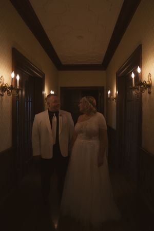 A couple shares a romantic moment in an elegant hallway illuminated by wall sconces.