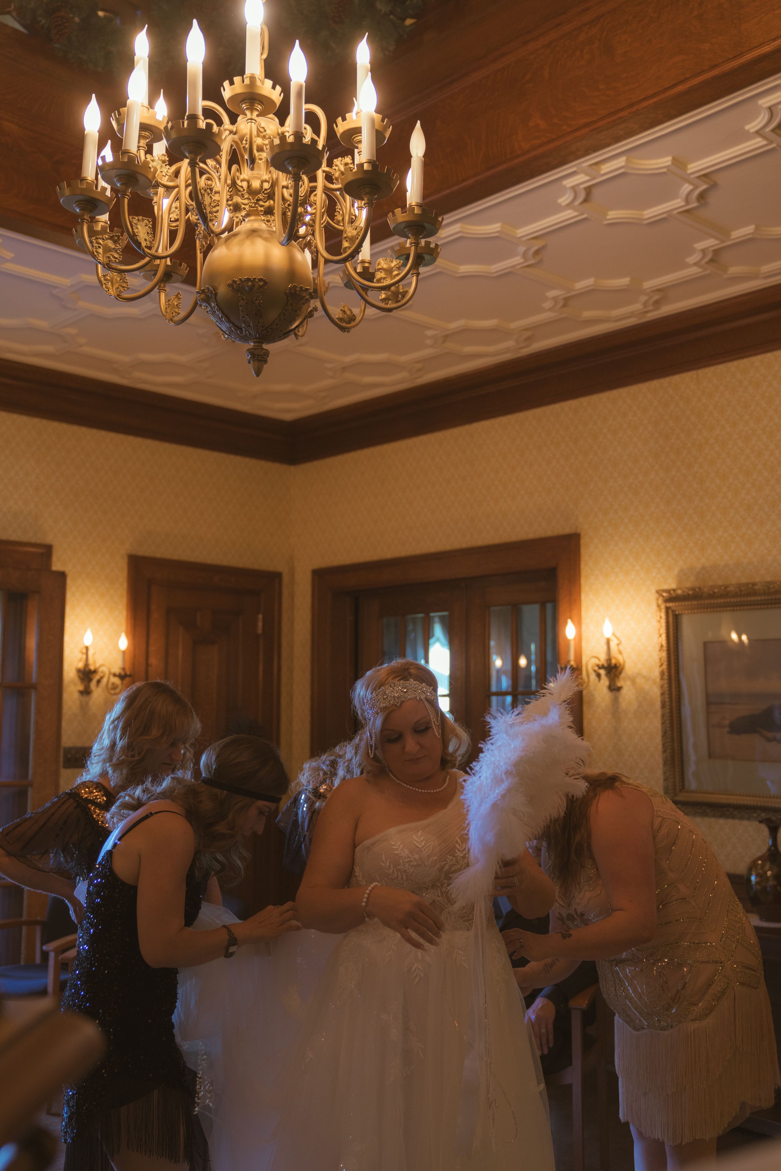 Wedding guests dance beneath crystal chandeliers in an ornate wood-paneled ballroom.