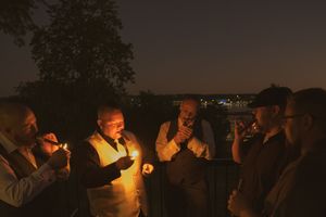 Group of wedding guests lighting cigars at dusk on outdoor patio.