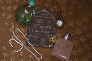 Wedding details including invitation and green glass decor on wooden surface.
