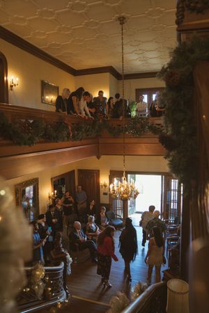 Wedding guests gather in an elegant two-story venue with chandelier and decorative garlands.
