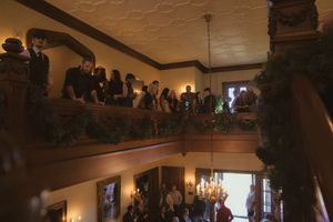Guests line the balcony of a dimly lit wedding venue with ornate ceiling details.