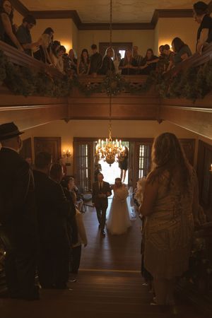 Wedding ceremony in progress under a crystal chandelier in a grand ballroom.