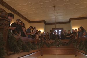Wedding guests observe from a decorated balcony in warm ambient lighting.