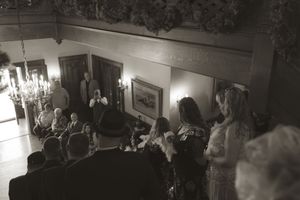 Black and white photo of wedding guests watching ceremony from above in historic venue.