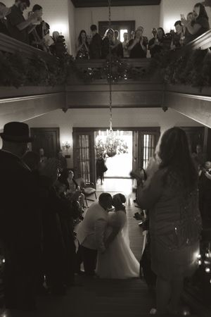 A wedding reception scene in a grand hall with guests watching a couple's first dance.