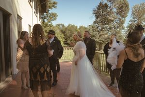 Wedding party poses together outdoors in front of a rustic building during golden hour.