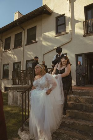Wedding party gathers on stone steps outside a white stucco building.