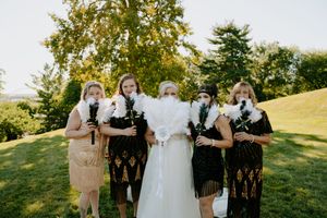 Wedding party stands in a line on grassy hillside with trees in background at sunset.