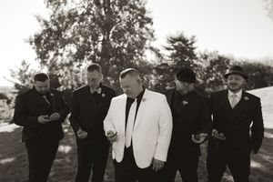 Wedding party in formal attire stands in line against bright sky.