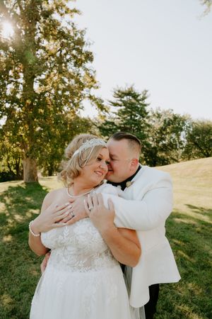 A tender moment between newlyweds captured in golden sunlight on a grassy hillside.