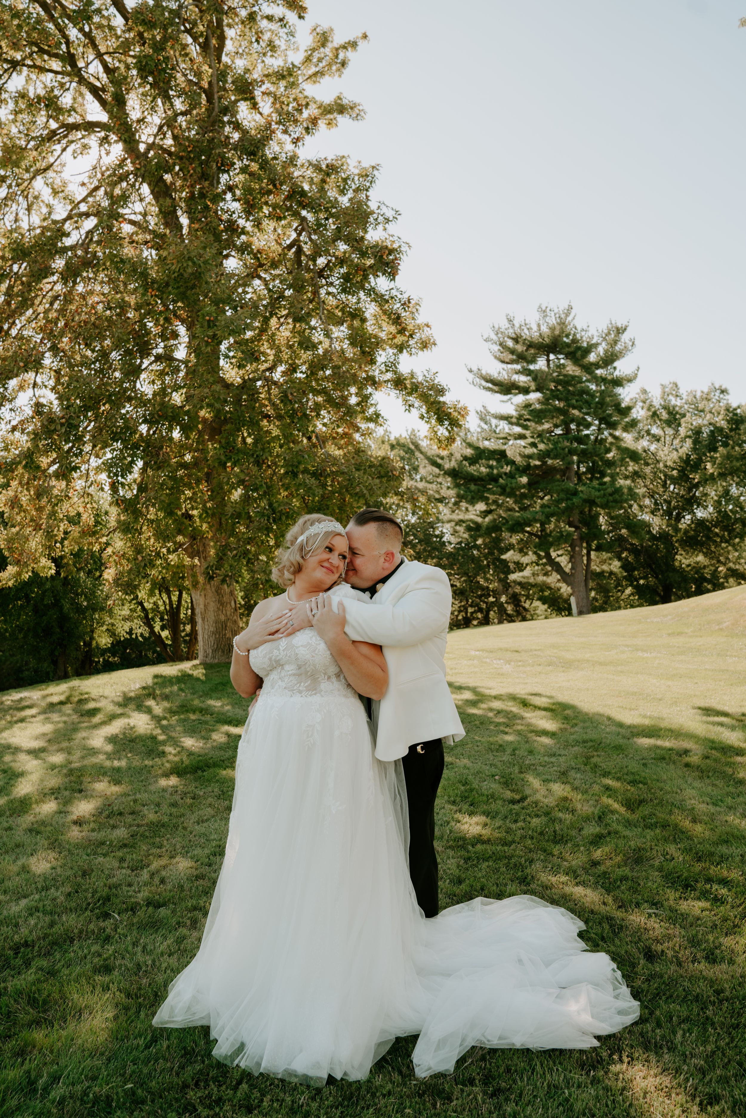A couple shares an intimate embrace during their wedding photoshoot on a sunny hillside.