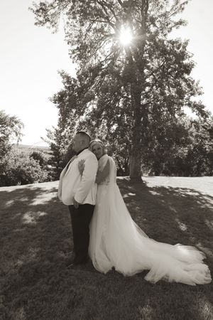 A black and white wedding portrait captures a couple's tender embrace on a grassy hillside.