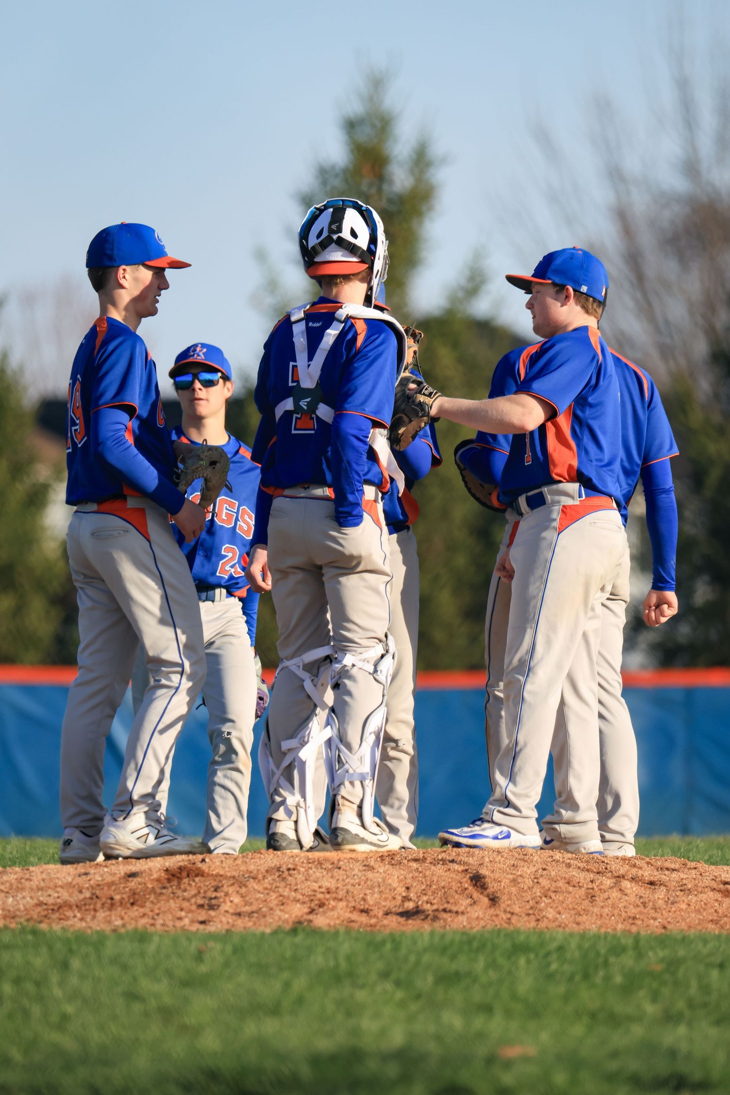 Baseball team huddles on pitcher's mound during game wearing blue and white uniforms.