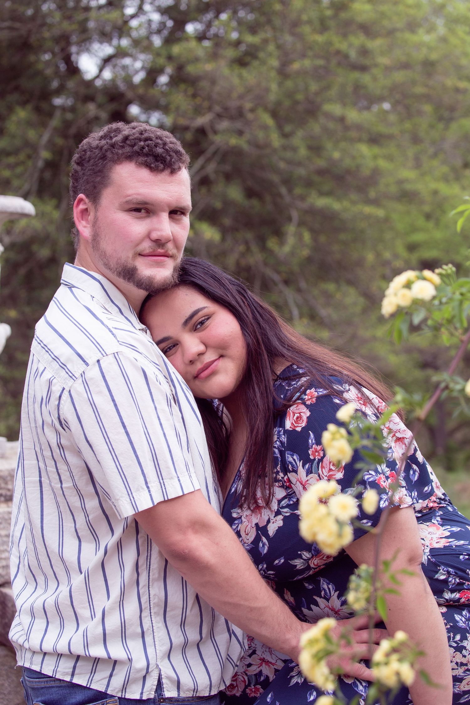 A couple embraces outdoors in nature while wearing casual clothing with yellow flowers in the foreground. At Maymont, RVA