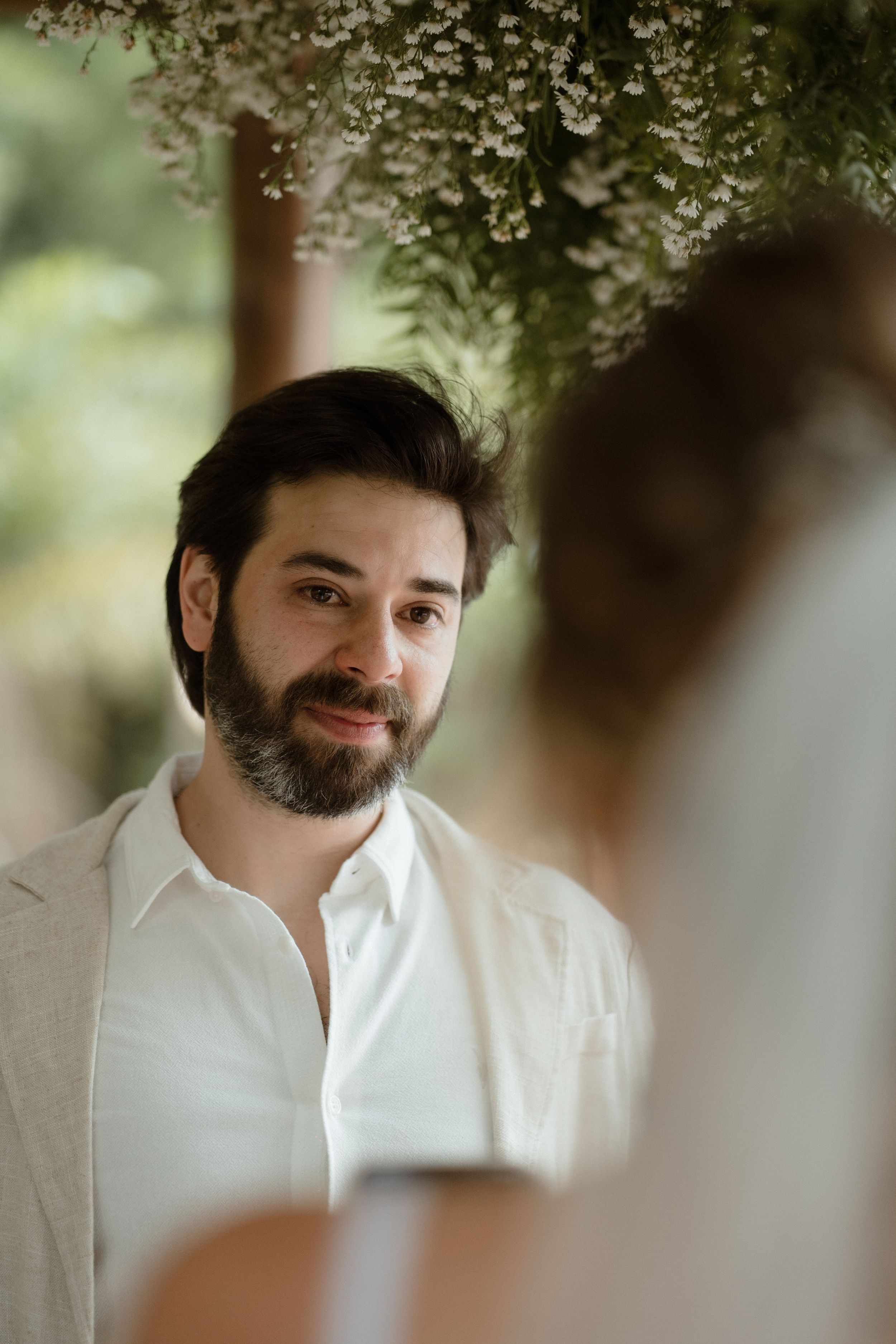 A close-up portrait shows a bearded man in white during an outdoor wedding.