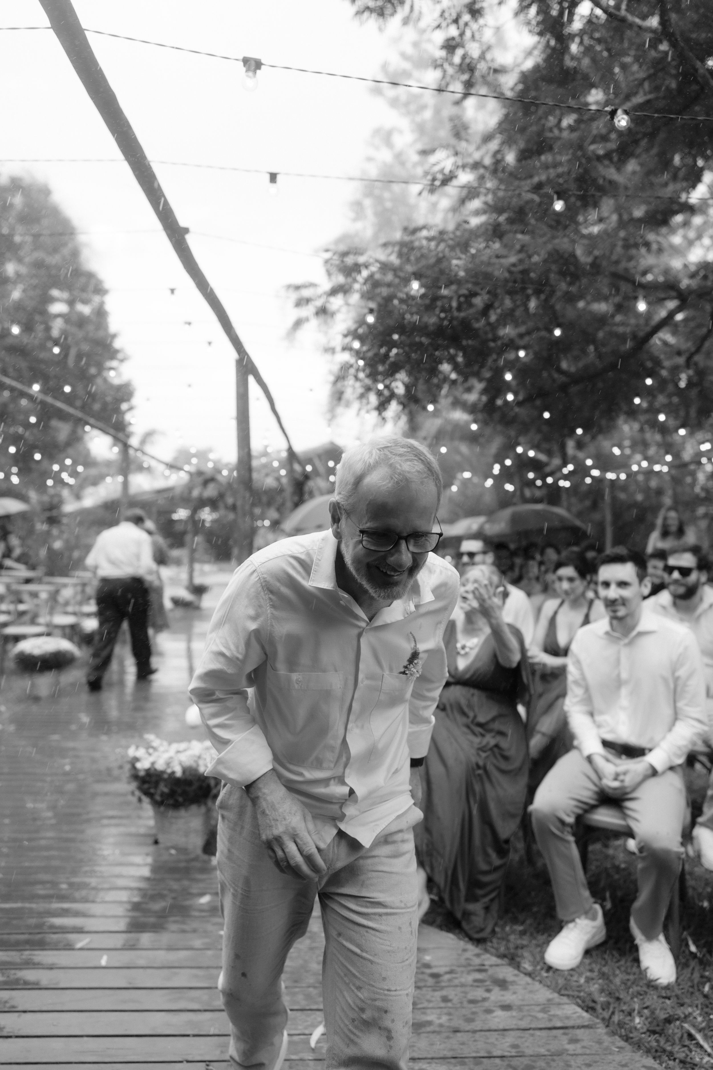 A candid black and white photo of guests enjoying a rainy outdoor wedding celebration.