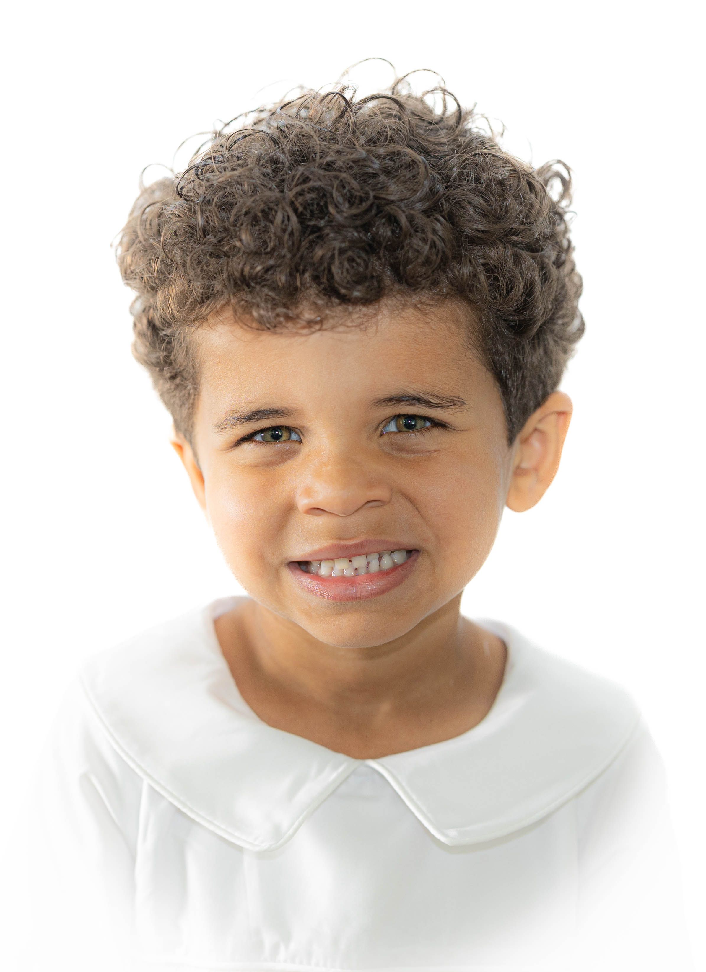 A child with curly hair wearing a white collared shirt smiles brightly at the camera.
