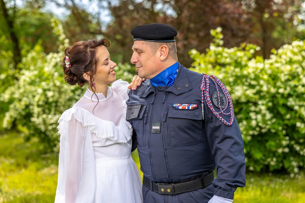 A couple embrace in a lush garden setting with blooming flowers in the background.