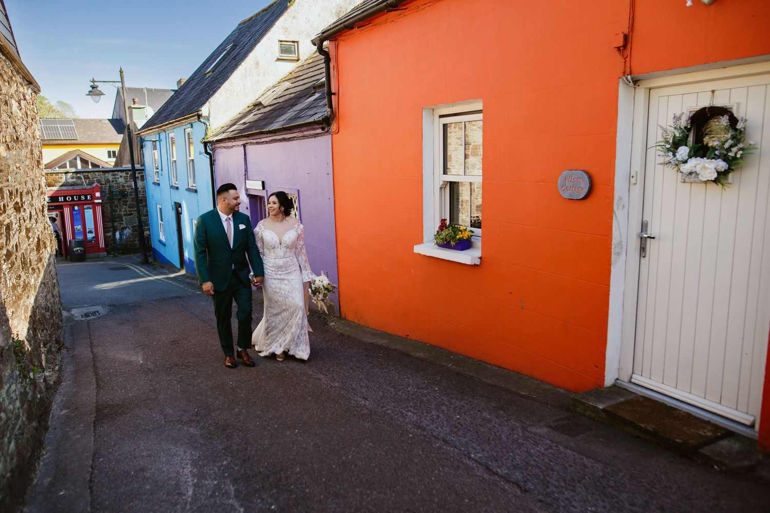 Wedding Elopement couple walking down colorful alley with bright orange and blue buildings in Kinsale, Ireland.