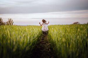Een witte jurk steekt af tegen een levendig groen tarweveld onder een stemmige lucht bij zonsondergang.