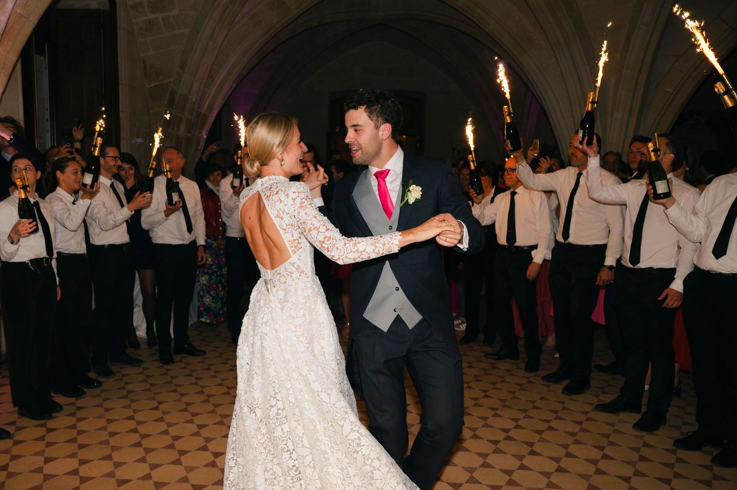 A couple's first dance at their wedding reception with sparkler-holding guests forming an aisle.